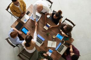 Menschen sitzen mit Laptops und Notizheften an einem Tisch